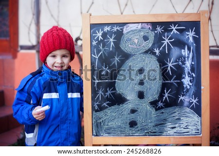 Adorable little boy, drawing winter picture with chalk on a board