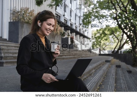 A woman in a black suit is sitting on a step with a laptop in front of her