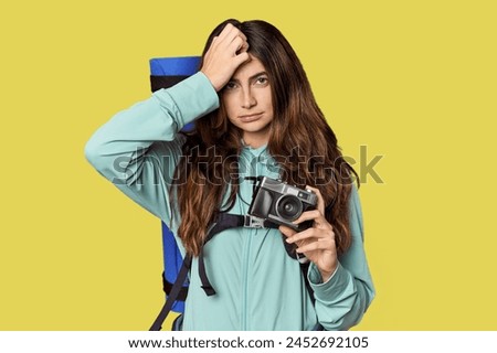 Caucasian woman with backpack and vintage camera being shocked, she has remembered important meeting.