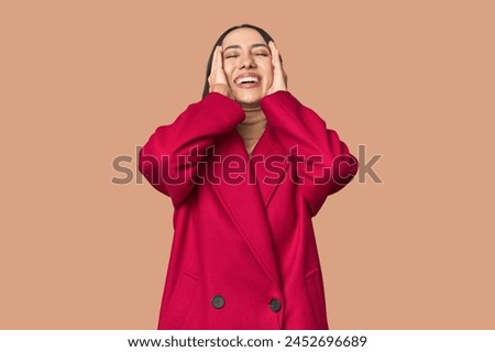 Modern young Caucasian woman portrait on studio background laughs joyfully keeping hands on head. Happiness concept.