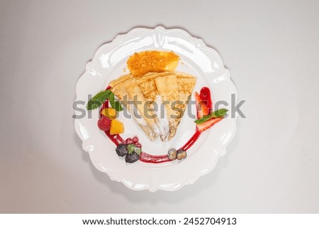Isolated image of a gourmet pancake on a white plate with red sauce and berries, perfect for food blogs or recipe websites.