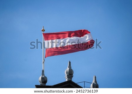 The waving flag of Dordrecht on top of the church in the historical city centre of Dordrecht. The flag has the same colours as the Austrian flag(red, white, red).