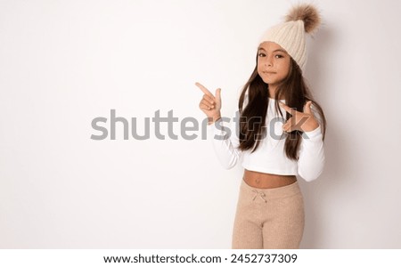 Brunette hispanic girl in winter hat showing and pointing up with fingers side while smiling confident and happy.