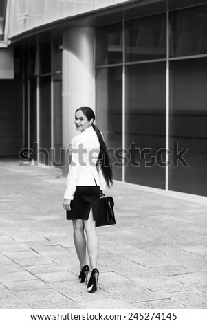 Confident business woman holding briefcase and walking in modern city.