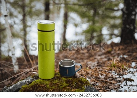 Camping utensils, thermos with a mug on the background of the autumn forest, camping utensils, thermo water bottle. High quality photo