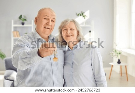 Happy senior couple holding a key in hands standing in the living room at home looking at camera enjoying real estate purchase, smiling and celebrating moving day. Relocating, mortgage concept. Royalty-Free Stock Photo #2452766723