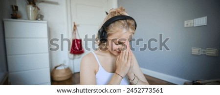 Close up portrait of young sporty woman in headphones, finish yoga training session, bowing with namaste hand sign, meditating.