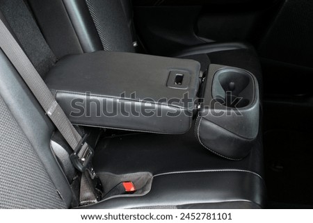 Armrest with cup holder inside. Leather comfortable black passenger seats and armrest. Black leather interior of the luxury modern car. Modern car interior details. Rear passenger seats. Royalty-Free Stock Photo #2452781101