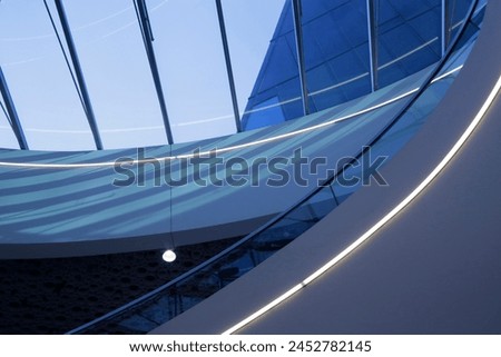 Close-up fragment of minimalist modern architecture with skylight in transparent roof. Ceiling windows above curvilinear interior structure of staircase and girders. Material geometric pattern.