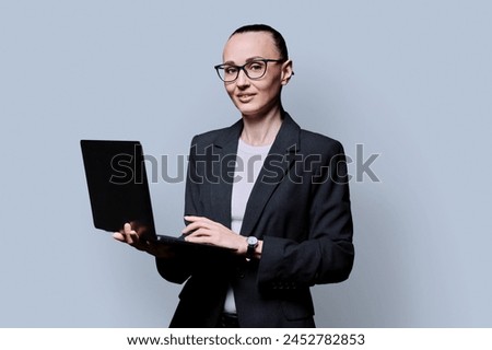 Middle-aged business confident woman using laptop on gray background