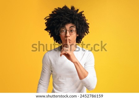 Black millennial guy showing silence sign, putting finger to lips, on orange studio background Royalty-Free Stock Photo #2452786159