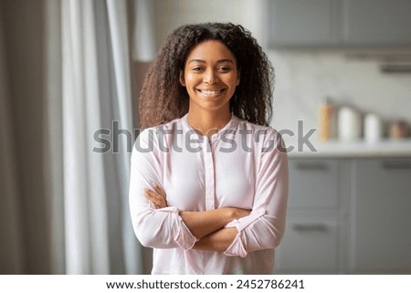 A confident african american lady stands with arms crossed in her home kitchen, showcasing independence and happiness Royalty-Free Stock Photo #2452786241