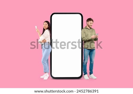 A man and a woman are standing next to an oversized smartphone screen on a pink background, mockup copy space