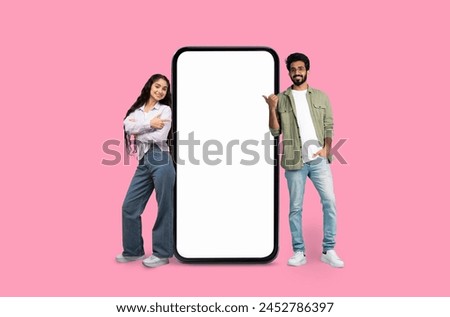 A young indian man and woman cheerfully presenting a smartphone mockup copy space on pink studio background