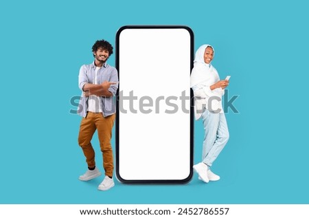 Multiracial man and woman in relaxed clothing posing alongside a giant smartphone mockup on a blue background