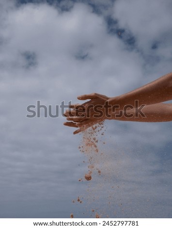 A person's hands are in the air, with sand falling from their fi