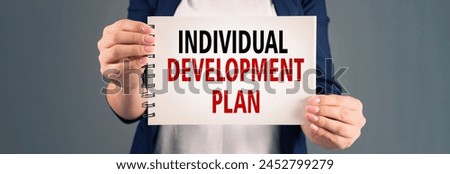 A woman holding a notepad with "individual development plan" written on it, on a gray background, stock photo