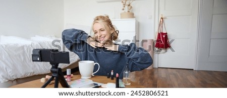 Lifestyle blogger records video of herself while doing hairstyle, showing makeup lifehacks for social media followers, vlogging, using camera for her blog, sitting in a room, drinking tea. Royalty-Free Stock Photo #2452806521