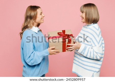 Side view elder amazed parent mom 50s years old young adult daughter two women together wear casual clothes hold present box with gift ribbon bow isolated on plain pink background. Family day concept