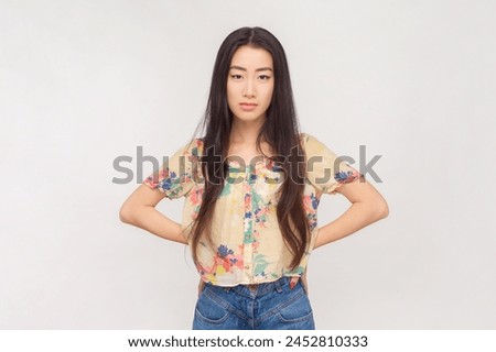 Portrait of serious strict unsmiling woman with long brunette hair standing with hands on hips looking with bossy expression. Indoor studio shot isolated on pink background. Royalty-Free Stock Photo #2452810333