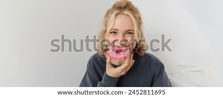 Portrait of cute blond girl holding pink doughnut with sprinkles on top, showing her favourite food.