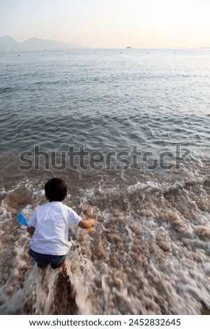 Hong Kong, Asia - 04 24 2011 : Exterior photo view of a ocean sea landscape holiday destnation with a young kid child children boy 5 years old jumping in water waves in warm orange evening sunset