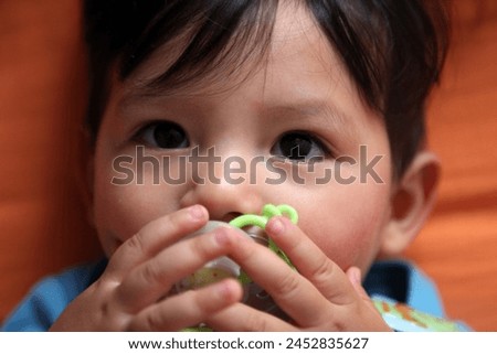 Interior photo view of an handsome cute good looking eurasian asian chinese 1 year old baby toodler kid child babe children boy portrait top view on a orange bed in blue clothes wiht a pacifier dummy