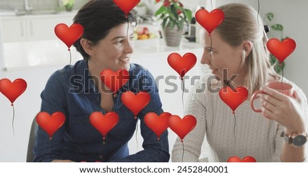Image of heart balloon emojis over happy caucasian female couple in love drinking coffee. Love, romance and celebration concept digitally generated image.