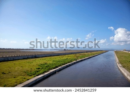 a river flows through a field with a bridge in the background