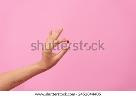 female hand delicately holds a white pill between fingers against a pink isolated background, symbolizing healthcare, dietary supplements, and treatment for conditions such as depression and diseases
