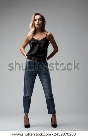 Full-length shot captures the young woman's effortless poise in a lace top, faded jeans, and high heels stance Royalty-Free Stock Photo #2452870253