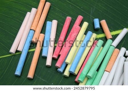 Chalk. Colored Chalk. Colorful chalk pastels in pile, on green tropical leaf background. Rainbow Spectrum of Colors. Colored chalk of soft pastels. Artist's Medium. Artwork. Artist Tools. Art Project.