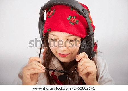 Portrait of young girl in red scarf, large headphones with microphone and black glasses. Woman who is radio or television presenter in the workplace. Funny female telecom operator. Freelancer at work