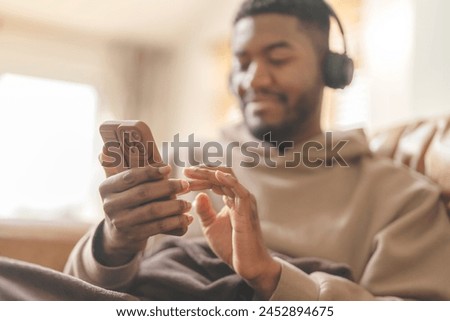 Happy man in brown hoodie  using phone, studying, learning, shopping, working online, talking, listening to music, audiobook, podcast while sitting on a safa at home Happy time at home concept