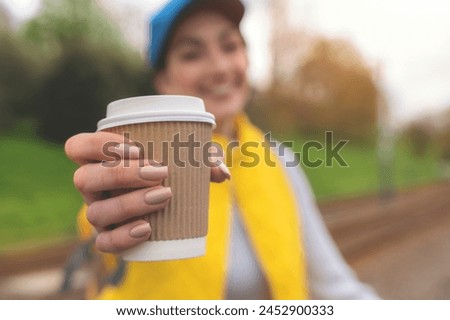 happy young woman in yellow waistcoat and blue cap drinking take away coffee, tea on the street and having fun time. lifestyle concept