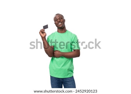 A 30-year-old American man dressed in a light green basic T-shirt holds a plastic credit card