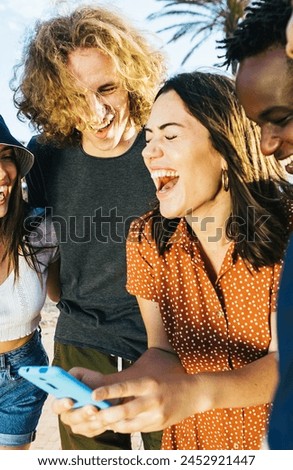 Vertical photo of young group of people having fun while watching social media content. Diverse happy millennial friends using mobile phone during vacation. Technology lifestyle and holiday concept.