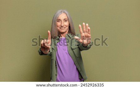 senior woman smiling and looking friendly, showing number six or sixth with hand forward, counting down Royalty-Free Stock Photo #2452926335