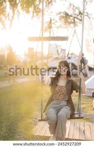 asian woman sitting in swing at camping site. sunset time