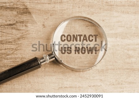 CONTACT US NOW word inscription visible through a magnifying glass on an old faded background