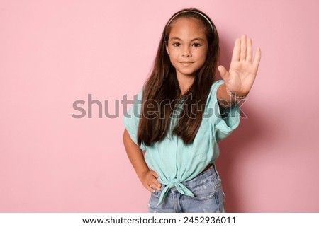 Young beautiful child girl wearing casual t-shirt standing over isolated pink background with open hand doing stop sign with serious and confident expression, defense gesture