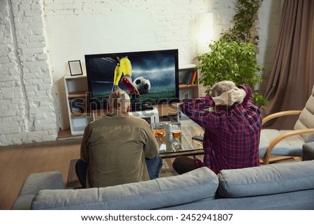 Tense game moment. Back view of two men sitting on sofa and watching online football match translation on TV. Concept of sport, championship, leisure and entertainment