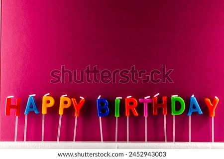 A row of colorful candles with the word Happy Birthday written in the middle. The candles are arranged in a line, with some of them being taller than others. Scene is celebratory and festive