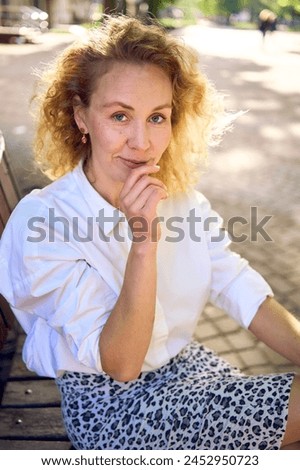 beautiful middle age woman in 70s, 80s style clothes on a bench in a sunlit avenue