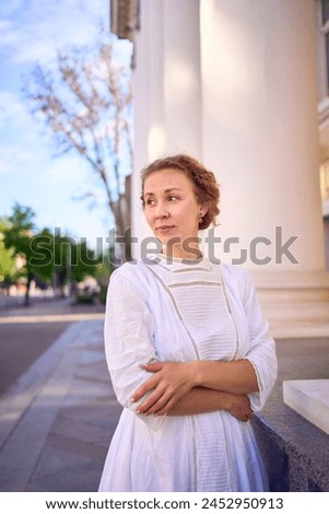 an elegant middle age woman in white vintage dress near theater with antique colonnades