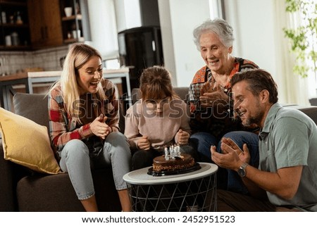 Heartwarming scene unfolds as a multi-generational family gathers on a couch to present a birthday cake to a delighted grandmother, creating memories to cherish Royalty-Free Stock Photo #2452951523