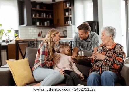 Heartwarming scene unfolds as a multi-generational family gathers on a couch to present a birthday cake to a delighted grandmother, creating memories to cherish Royalty-Free Stock Photo #2452951527