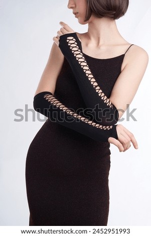 Cropped close-up shot of a girl in a black dress with black long fingerless gloves. A girl in black openwork mittens is posing on a pastel background. Front view. Royalty-Free Stock Photo #2452951993