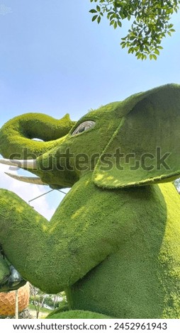An elephant statue surrounded by green grass stands tall in the sun