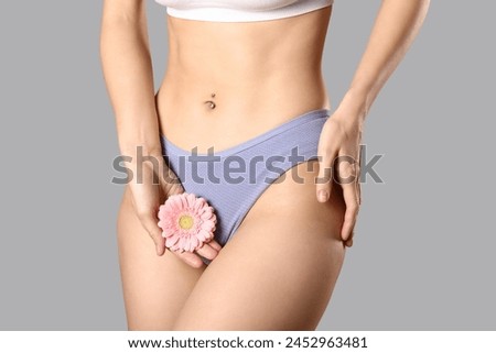 Young woman in panties with beautiful pink flower on grey background Royalty-Free Stock Photo #2452963481